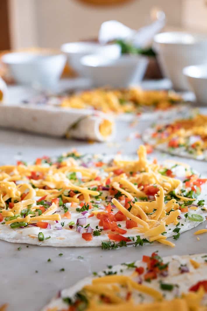 Tortillas topped with brightly coloured diced vegetables and cheddar cheese.