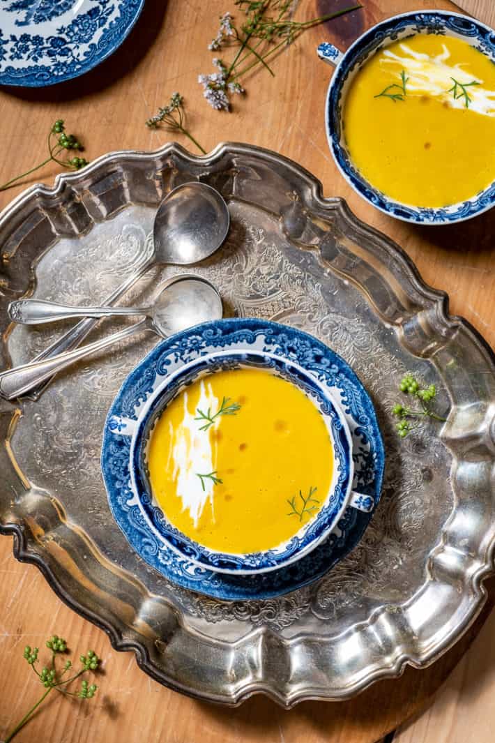 Carrot ginger soup served in transferware soup bowl with handles, on a silver tray.