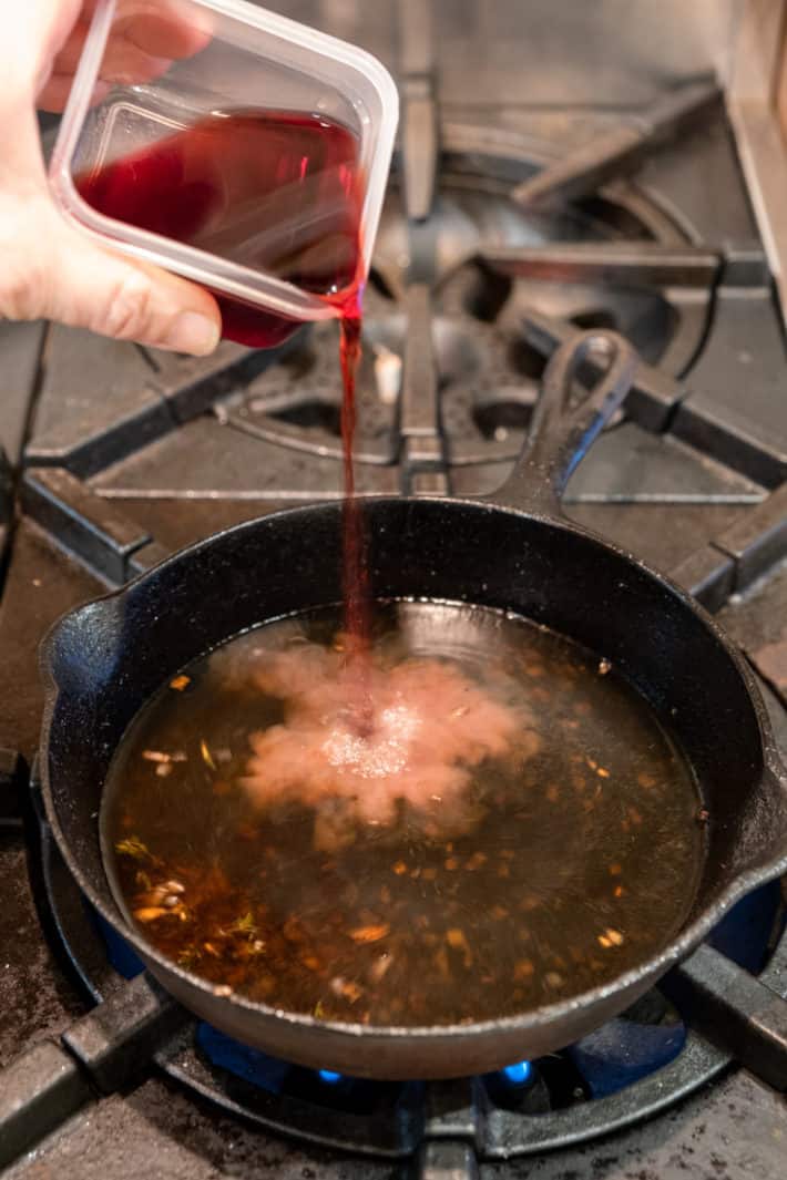 Pouring 1/2 cup of red wine into a small cast iron pan to make a sauce.