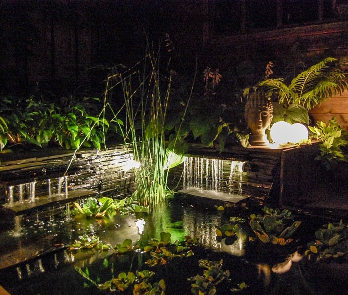 Glowing outdoor orbs in garden above lit up waterfall in backyard pond.