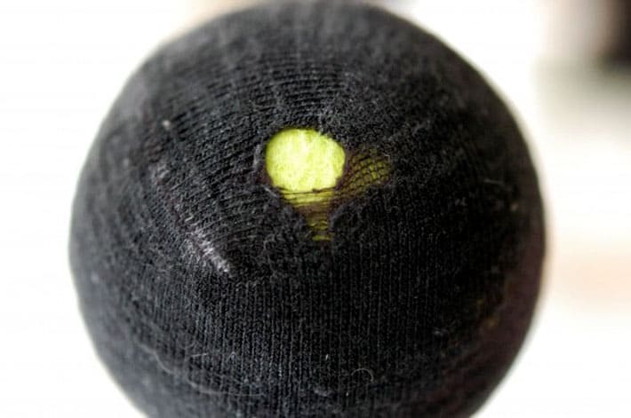 Black sock with hole stretched over yellow tennis ball.