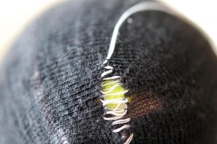 How to darn a sock. Black sock over yellow tennis ball being darned with white thread in criss cross pattern.