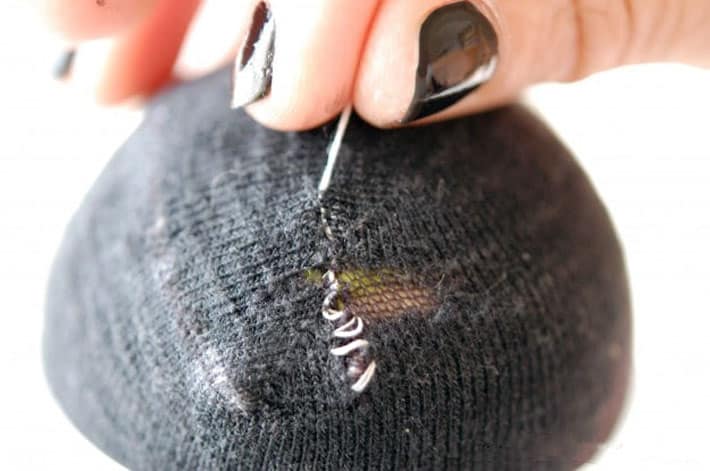 Black sock over yellow tennis ball being darned with white thread.