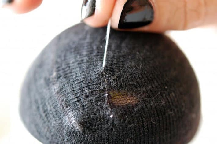 Black sock over yellow tennis ball being darned with white thread. Thread is pulled tight to close up hole.