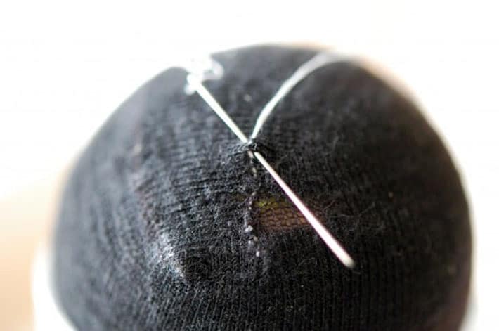 Black sock over yellow tennis ball being darned with white thread. Finishing mend by making a knot.