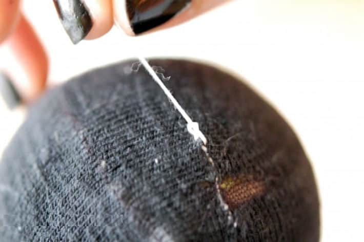 How to darn a sock. Black sock over yellow tennis ball being darned with white thread. Finishing mend by making a knot.