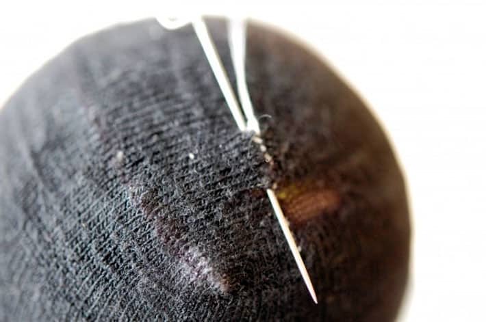 How to darn a sock. Black sock over yellow tennis ball being darned with white thread. Finishing mend by making a knot.