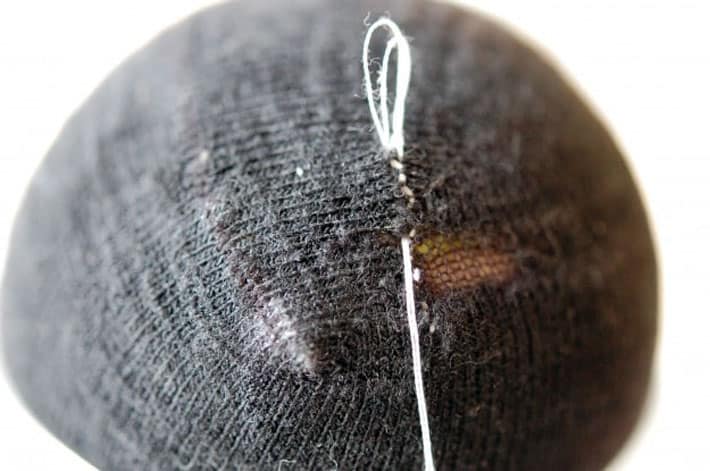 Black sock over yellow tennis ball being darned with white thread. Finishing mend by making a knot.