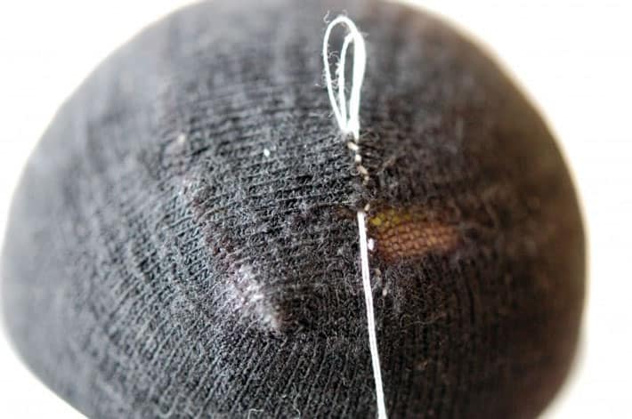 How to darn a sock. Black sock over yellow tennis ball being darned with white thread. Finishing mend by making a knot.