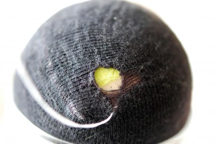 Black sock over yellow tennis ball being darned with white thread.