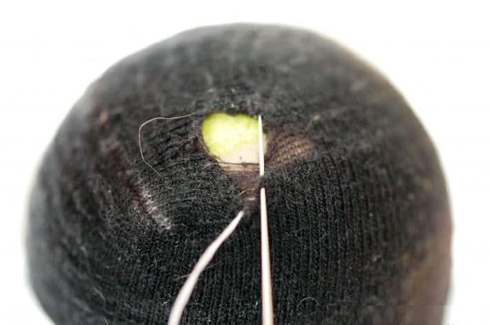 Black sock over yellow tennis ball being darned with white thread.