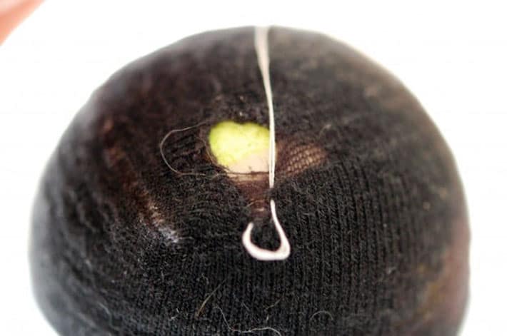 Black sock over yellow tennis ball being darned with white thread.