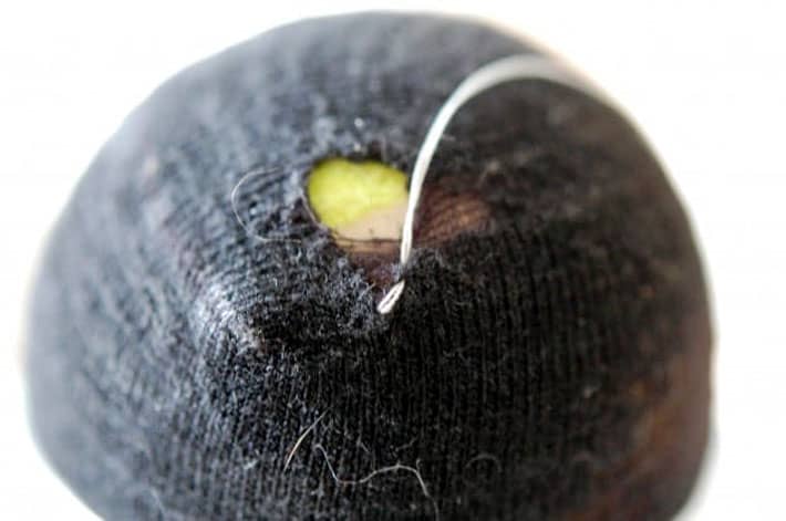 Black sock over yellow tennis ball being darned with white thread.