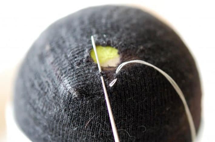 Black sock over yellow tennis ball being darned with white thread.