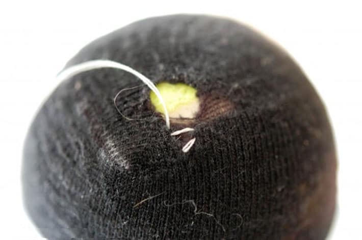 Black sock over yellow tennis ball being darned with white thread.