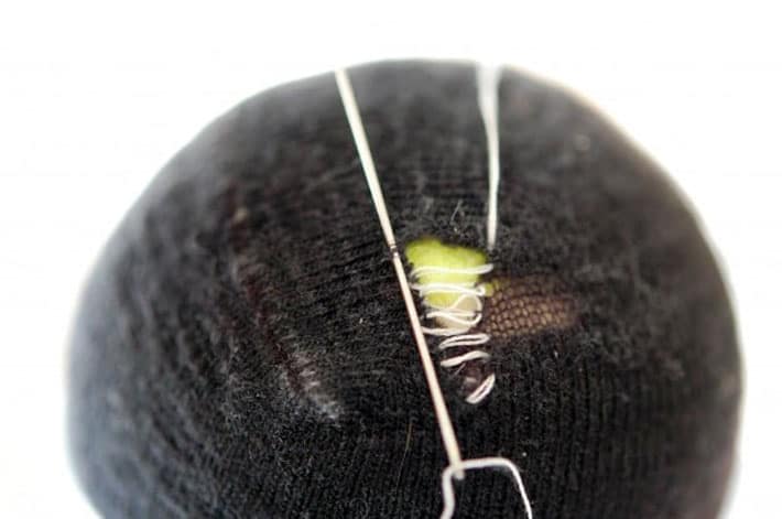 How to darn a sock. Black sock over yellow tennis ball being darned with white thread.