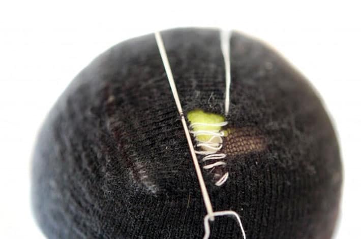 Black sock over yellow tennis ball being darned with white thread.