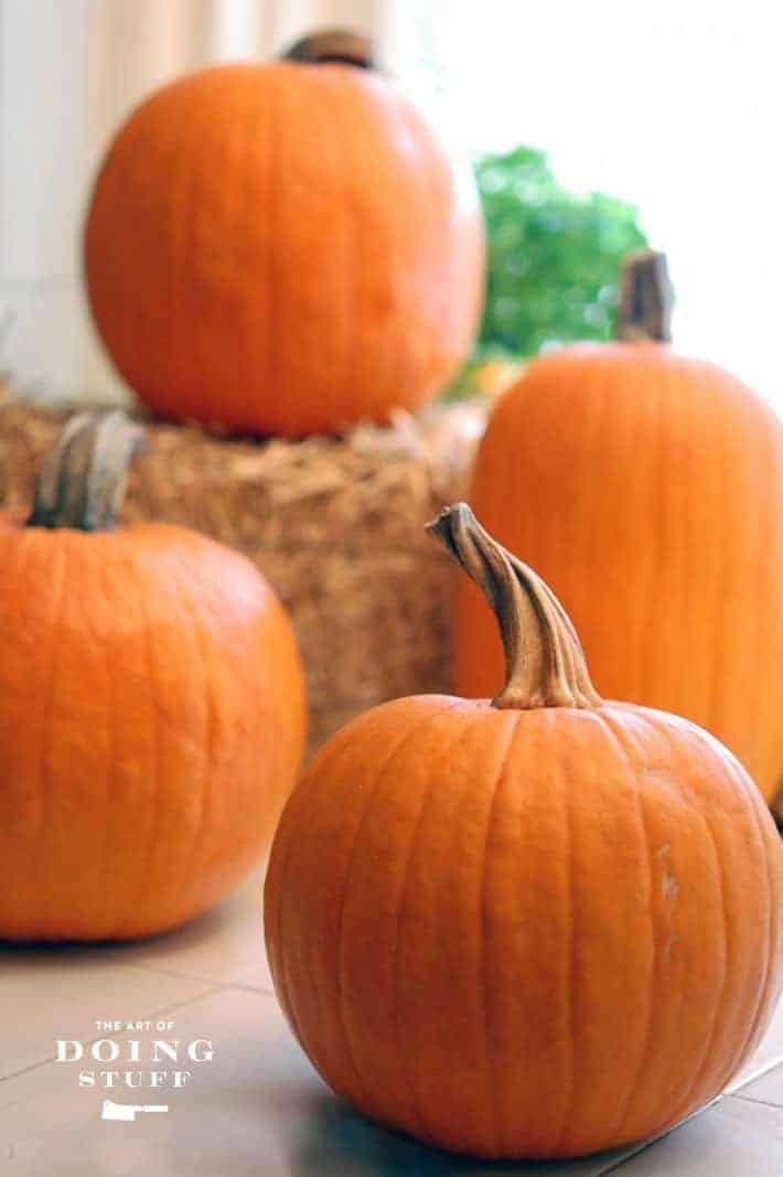 4 pie pumpkins on a countertop with a small bale of straw.