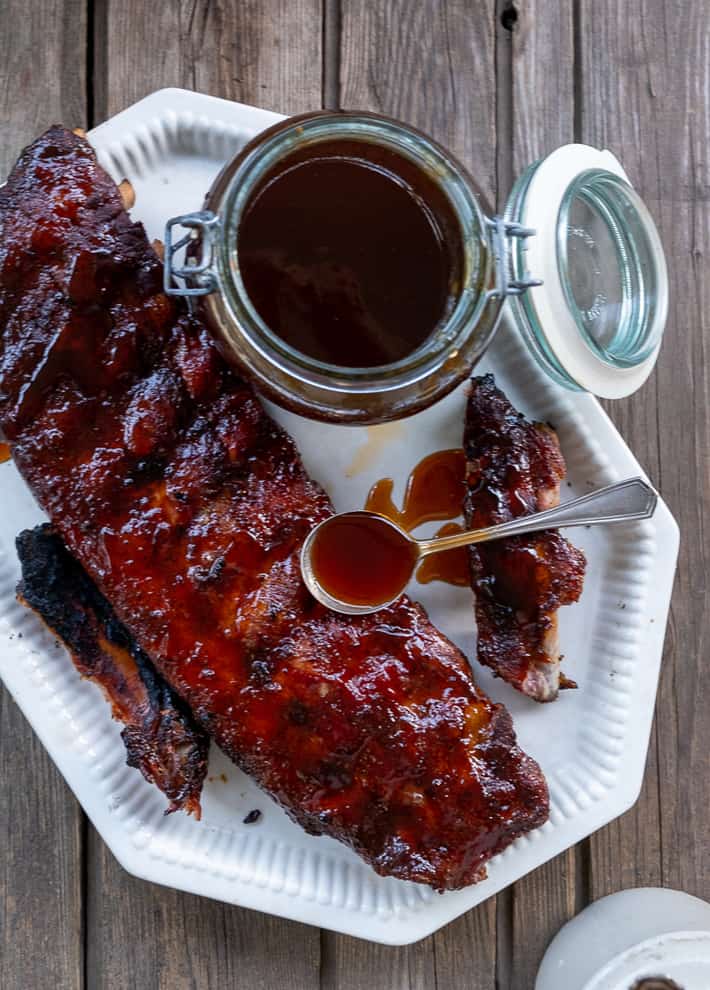 Smoked spare ribs on a white platter with maple bourbon bbq sauce dripping from a spoon.