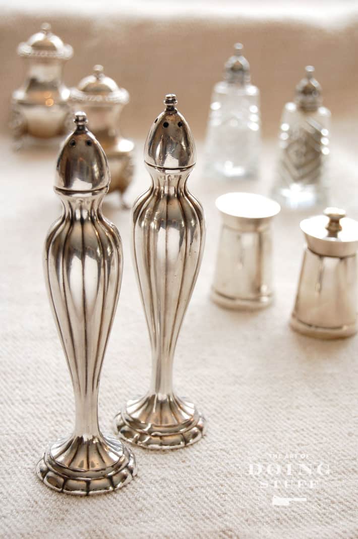 Tall, slender antique silverplate salt and pepper shakers on natural linen tablecloth, various other vintages shakers in background.