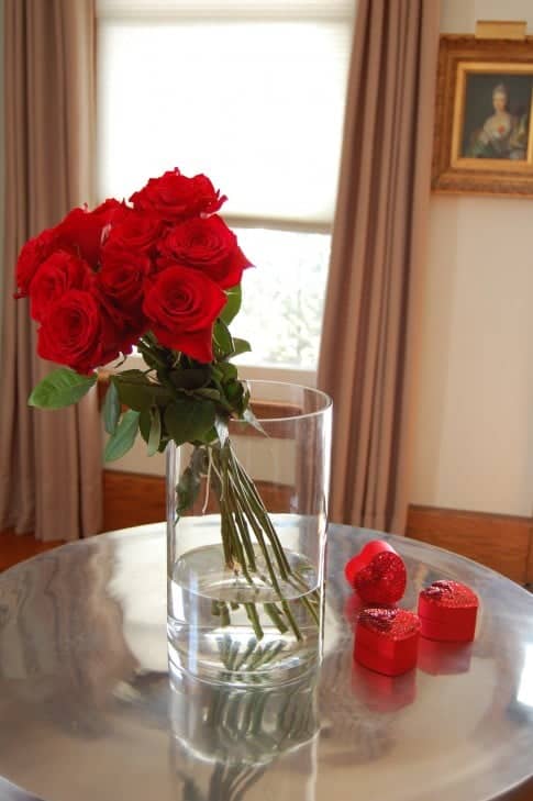 Contemporary arrangement of a dozen red roses in a glass cylinder vase on a stainless steel round table.