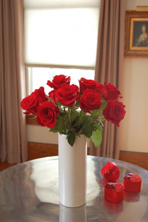 A dozen red roses in a white, narrow cylinder vase. Shows off how a smaller vase mouth helps to keep roses upright and in place.