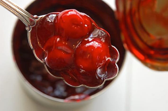 Cherry pie filling with 3 cherries sitting on scalloped, antique spoon.