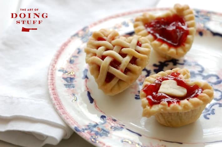 Beautiful cooked mini cherry tarts in the shape of hearts on an antique flow blue plate with white napkin.