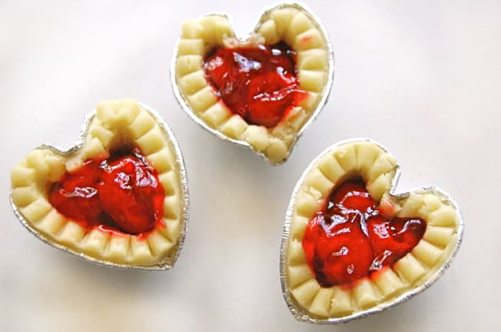 Mini frozen tart shells filled with cherry pie filling on white counter.