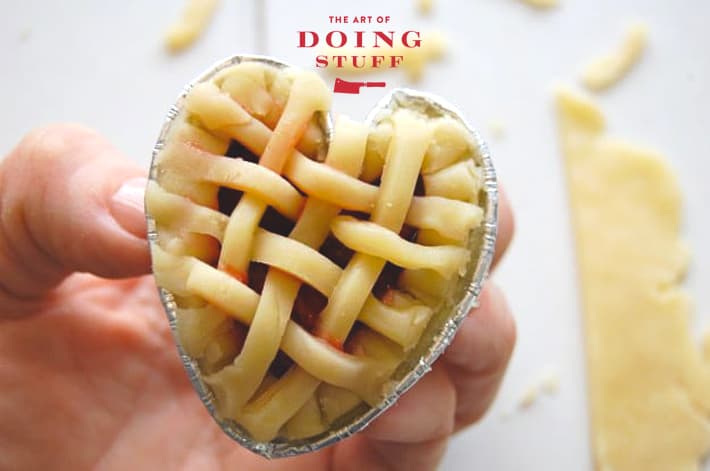 Hand holding up mini cherry tart with tiny lattice crust work on top of it.