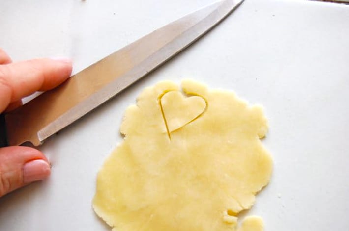 Rolled out pie dough on white counter with heart shape cut out of it.