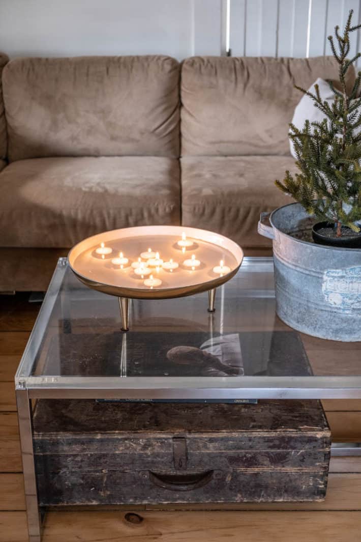 DIY floating tea lights in a modern bowl on a clear glass coffee table with rustic accents around.