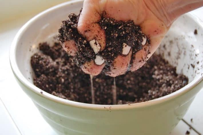 How to start vegetables from seed. A hand squeezes a palmful of sand with water streaming out of it showing too much moisture.