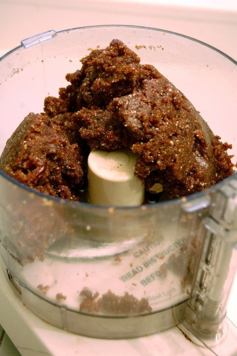 Dark brown dough ball in Cuisinart made from walnuts, dates, cranberries and other wholesome ingredients.