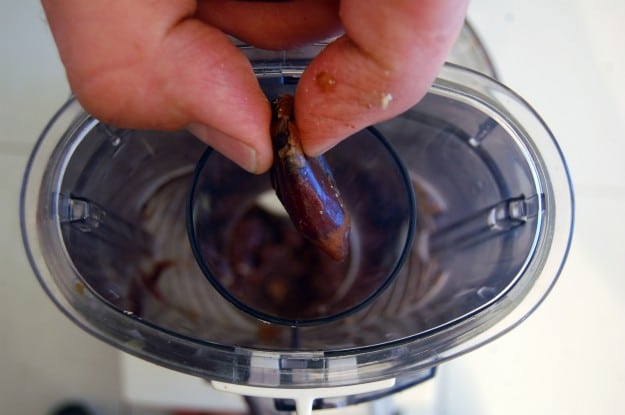 Overhead shot dropping dates into the chute of a food processor.