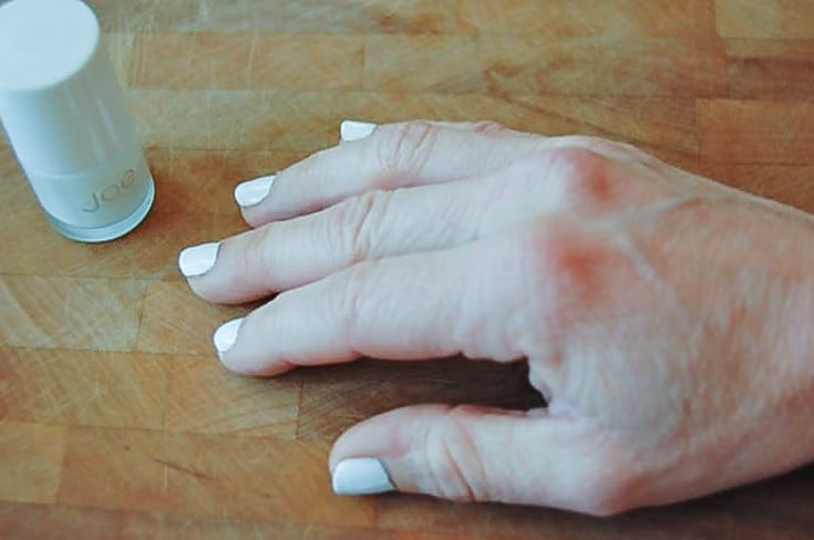 A woman's hand with white nail polish resting on a wood surface.