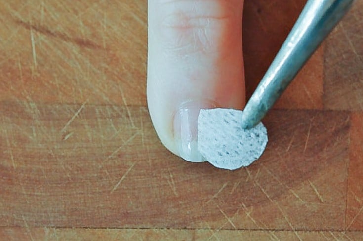 A small piece of teabag being lowered onto a fingernail by tweezers.