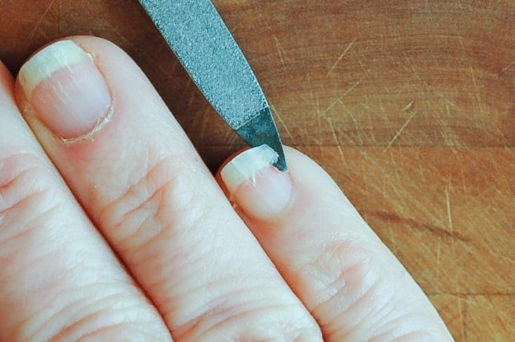 A woman's fingernail being lifted up with a nailfile at the point that it's broken.