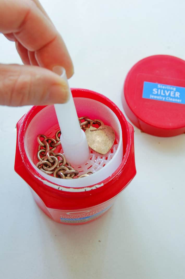 Lowering a silver bracelet into the red jar of silver dip to remove tarnish.