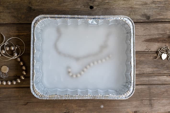 An aluminum pan with silver jewelry, hot water and sodium carbonate in it for cleaning tarnished metal.