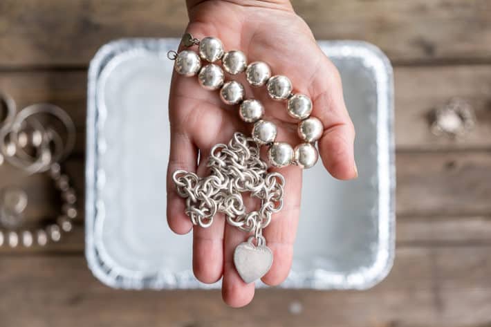 A woman's hand holds out a silver Tiffany heart necklace and silver bead necklace after being cleaned.