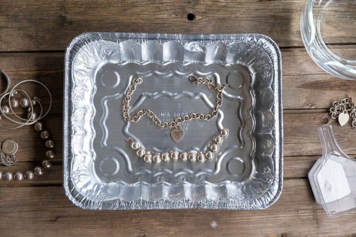 Two silver necklaces placed inside a common aluminum pan on a wood table.