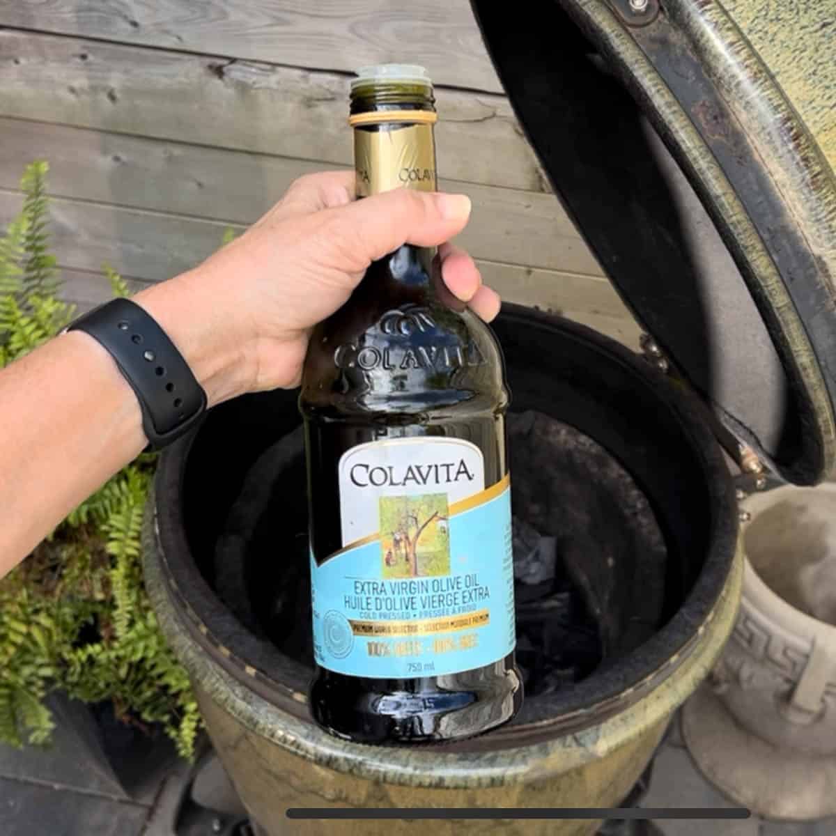 Bottle of olive oil held up in front of bayou classic smoker.