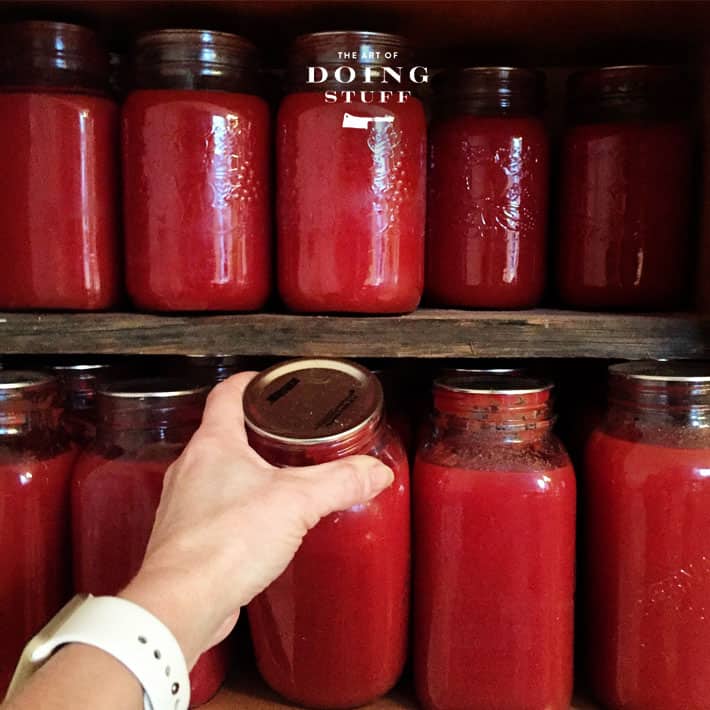 Rows of large mason jars filled with tomato sauce on rustic barn board shelves.