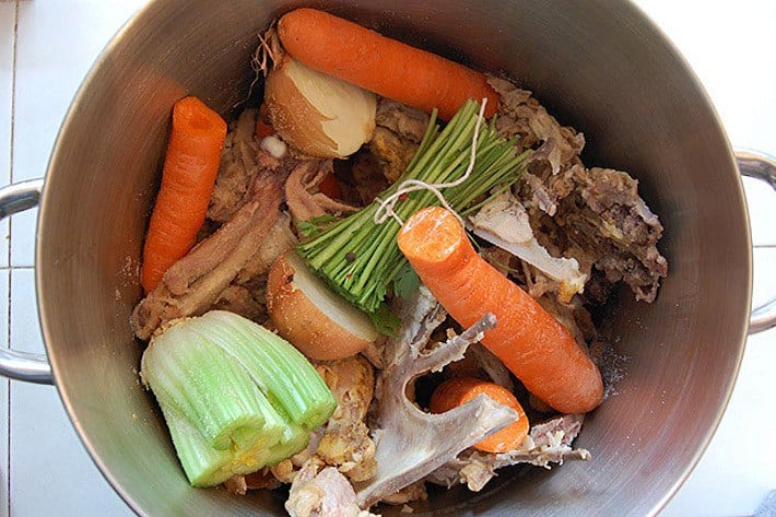 Overhead shot of a stock pot filled with chicken, whole carrots, parsley stems and other broth ingredients.