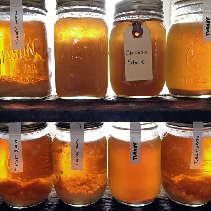 Rows of chicken and turkey broth on wood shelves with light behind them making them glow.