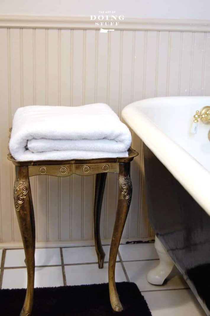 Fluffy white folded towel on a gold florentine table beside a clawfoot bathrub.