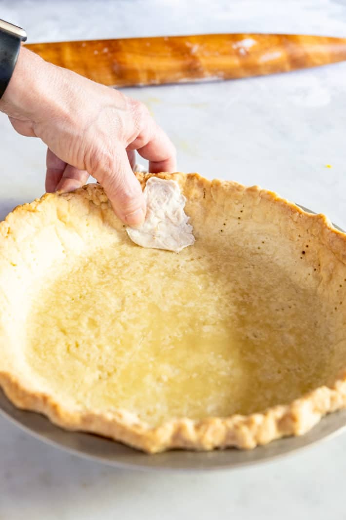 Fixing a crack in a baked pie crust by patching it with raw dough.