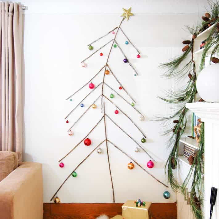 A tree made of twigs, flat against a wall from floor to ceiling complete with ornaments.