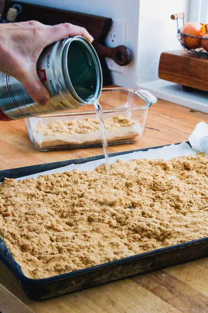 Pouring a tin of melted wax over a baking tray of sawdust.